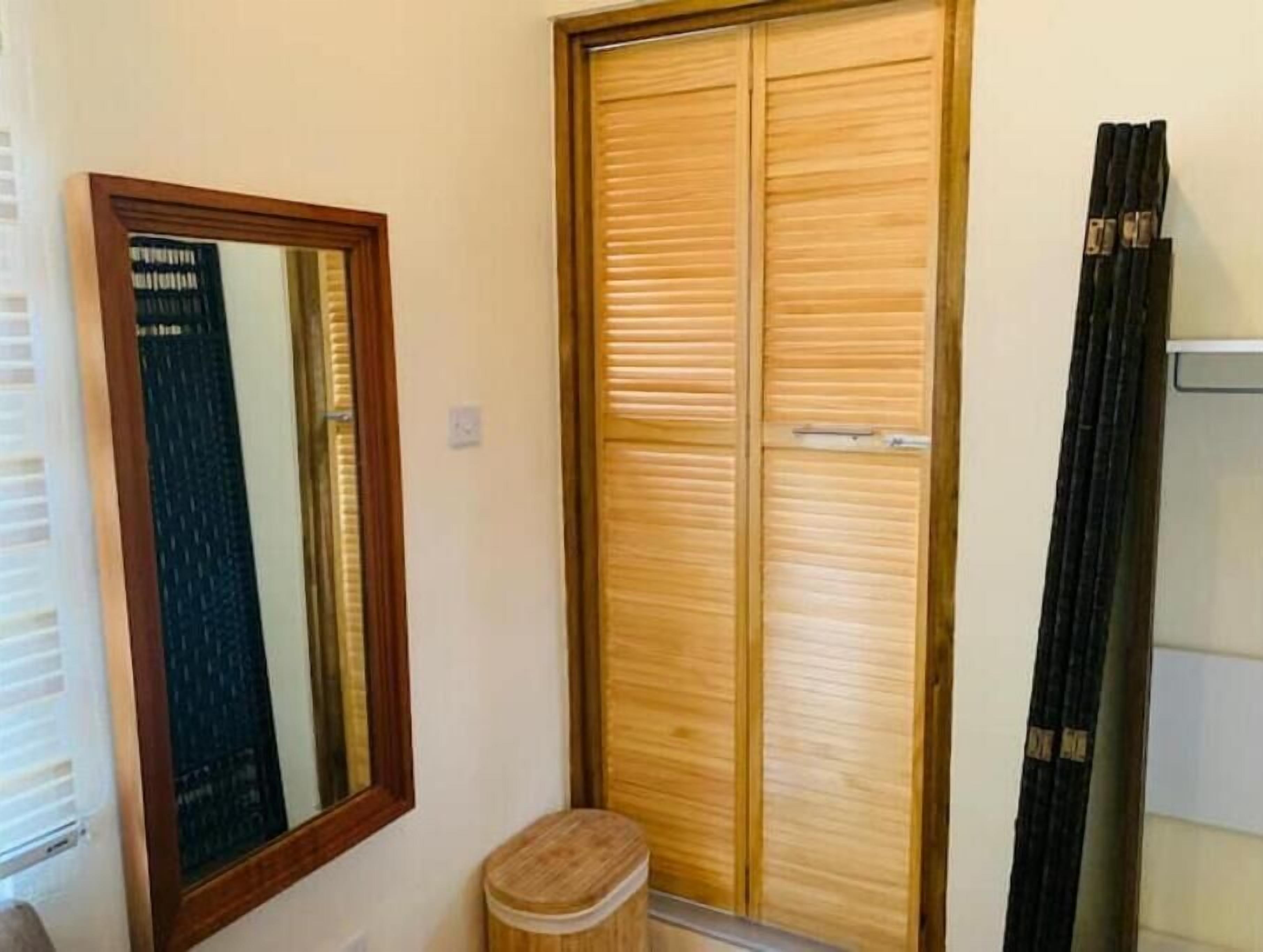 A wooden wardrobe with a mirror, a small stool, and a curtain.