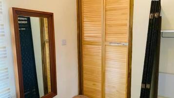 A wooden wardrobe with a mirror, a small stool, and a curtain.