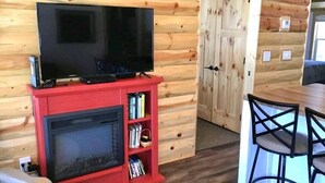 A cozy cabin interior with a television on a red stand, a fireplace, and a wooden door.