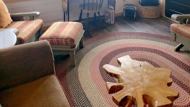 A cabin with a large window overlooking a lake, a wooden dining table with chairs, and a cozy seating area with a patterned rug.