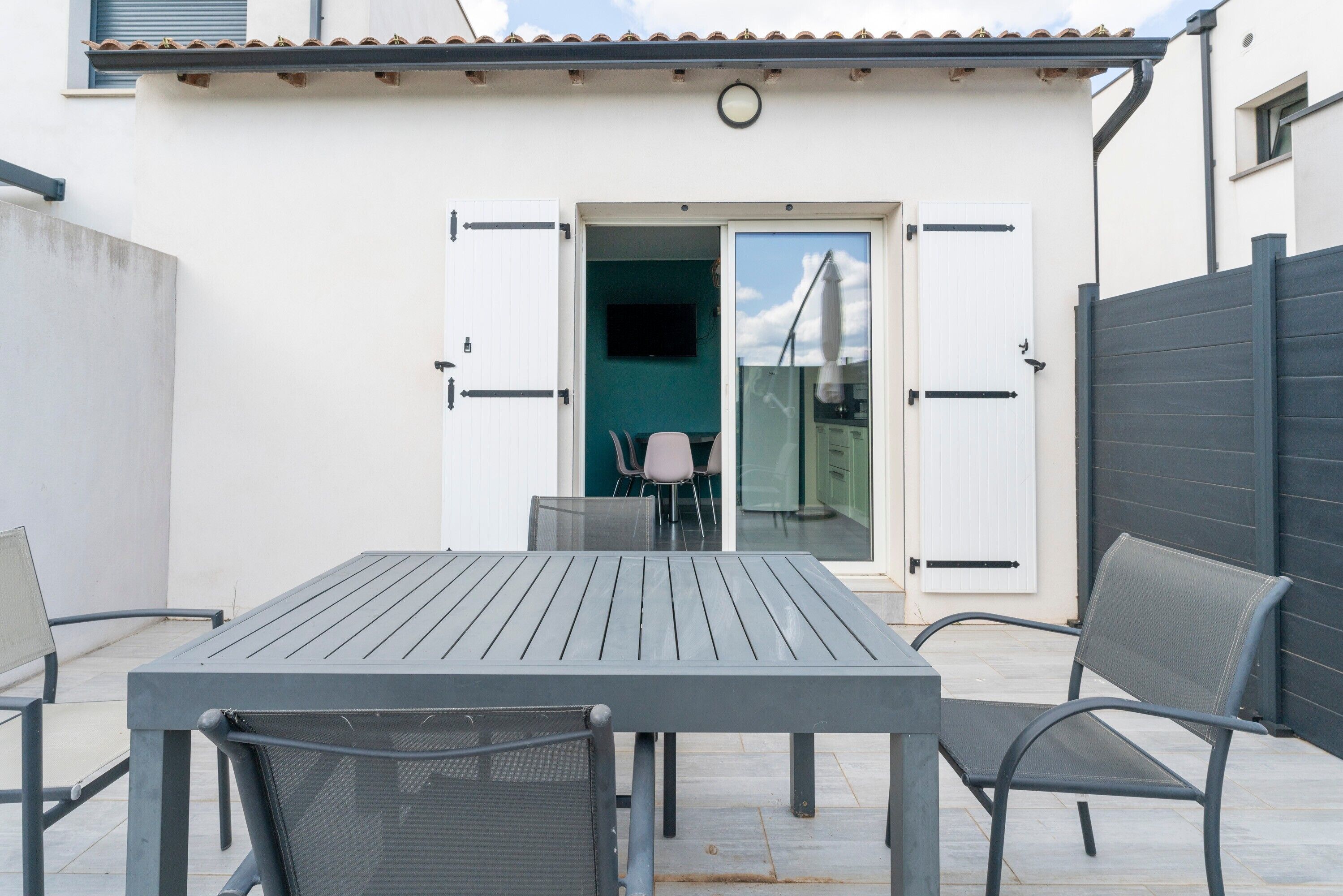 Une terrasse avec une table et des chaises, une porte-fenêtre coulissante et une vue sur l’intérieur.