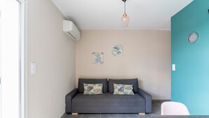 Una sala moderna con un sofá gris, dos obras de arte colgadas en la pared, un reloj y una lámpara colgante.