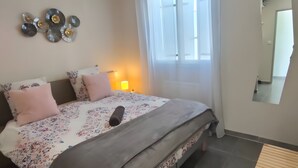 Un dormitorio con cama, mesita de noche, lámpara, decoración en la pared y una ventana con cortinas.