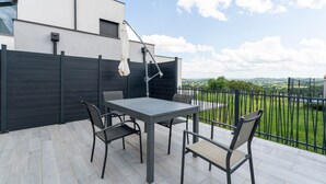 Un patio con una mesa y sillas, una valla negra, y vistas al campo.