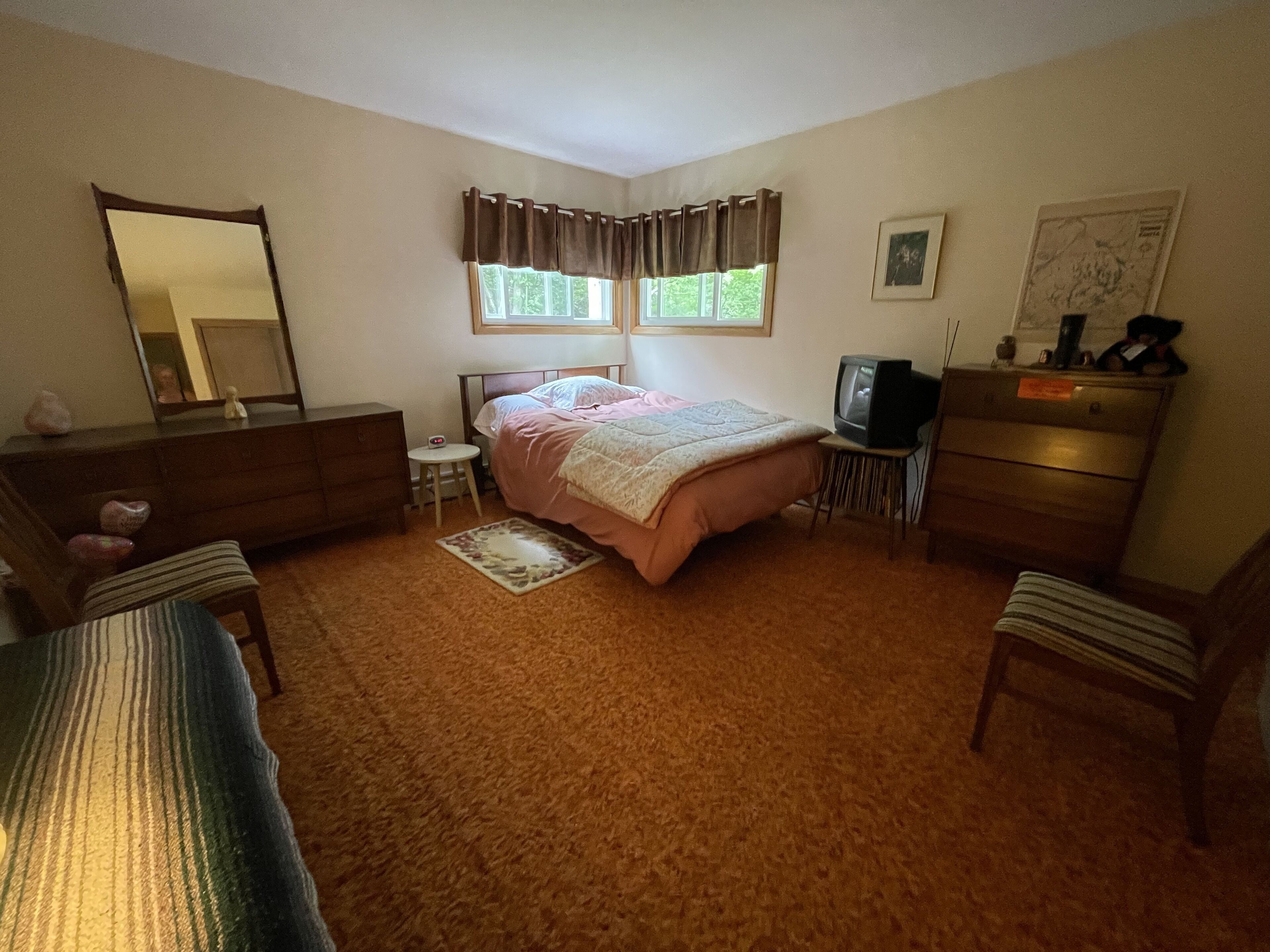 A bedroom with a bed, dresser, chair, television, and a small table.