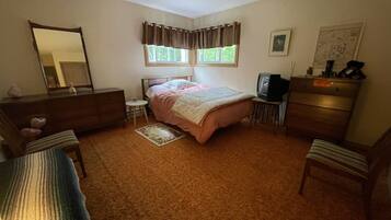 A bedroom with a bed, dresser, chair, television, and a small table.