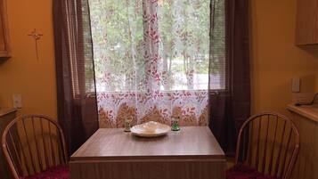 A dining area with a table and two chairs, a window with floral curtains, and a wall-mounted light fixture.