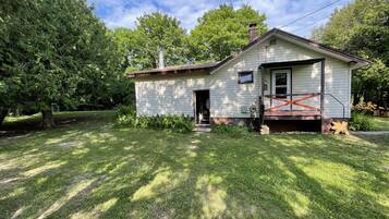 A small, single-story house with a front porch and a chimney, surrounded by a well-maintained lawn and trees.
