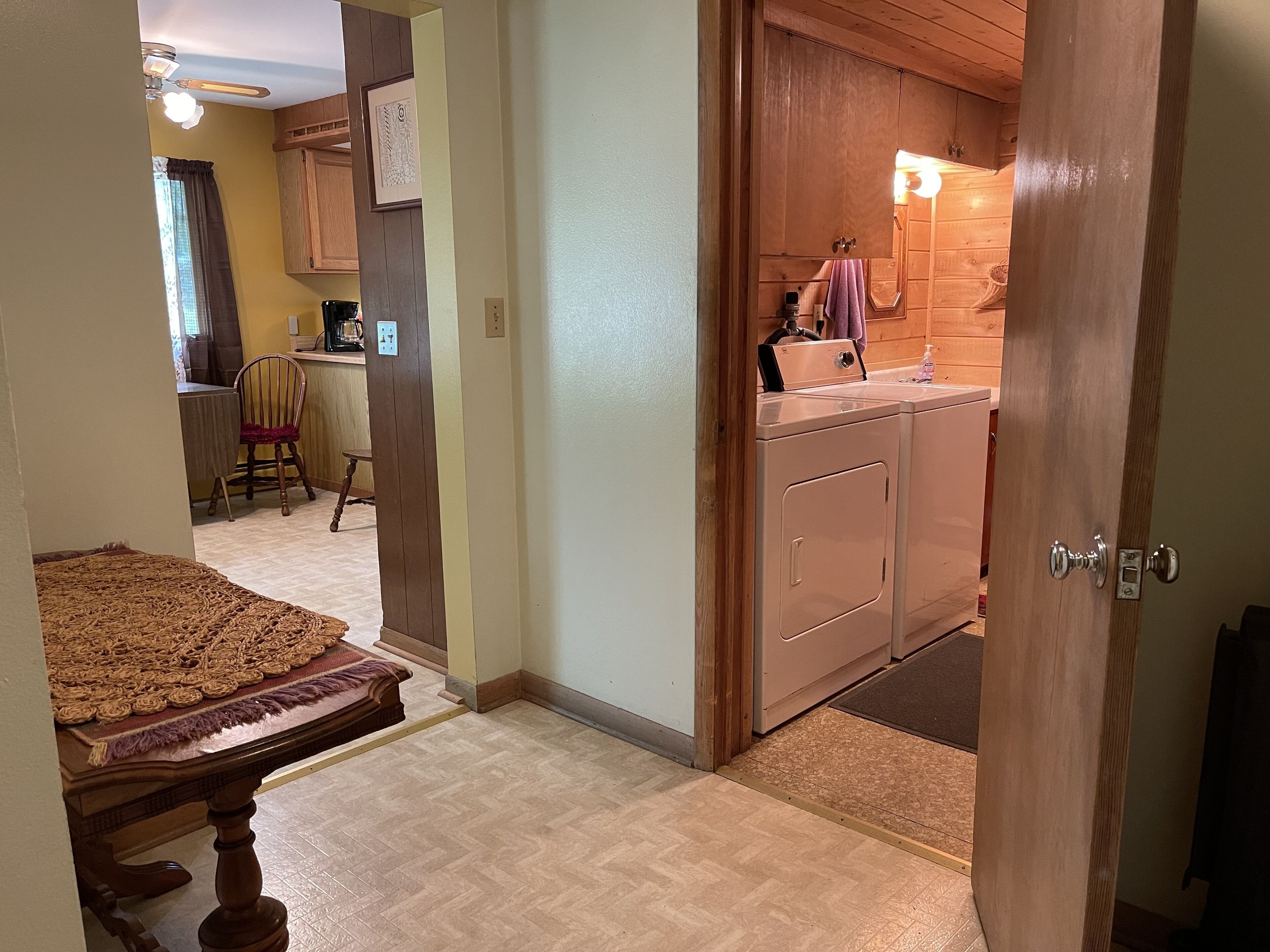 A hallway leading to a kitchen with wooden cabinets, a dining area with a table and chairs, and a laundry area with a washing machine.