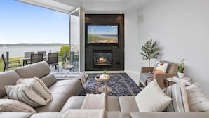A modern living room with a fireplace, a large TV, and a view of the outdoors. - Piermont Waterfront Villa! Sleeps up to 16 adults Luxuriously and In Style (Piermont)