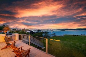 Una terraza con mobiliario exterior, una parrilla y vistas a un puerto deportivo y una masa de agua al atardecer.