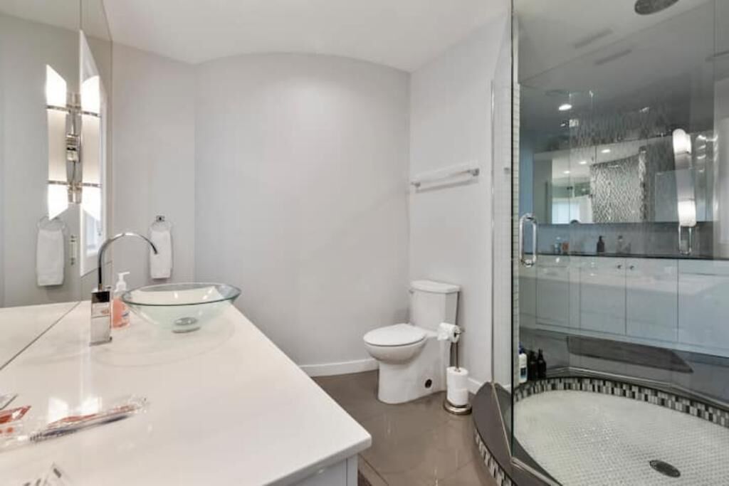 Ein modernes Badezimmer mit einer Duschkabine aus Glas, einem weißen Waschbecken mit Glasbecken und einer Toilette.