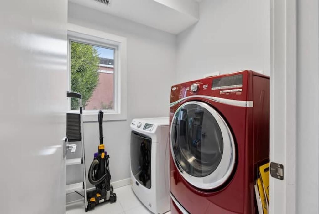 A laundry room with a red front-loading washer and dryer, a white wall, and a window with a view of a tree.