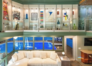 A spacious living area with a large sofa, a pool view, and a glass railing with artwork. - Skyline Villa Indoor Pool (Elkhorn)