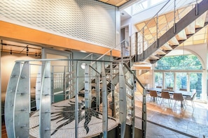 A modern interior with a spiral staircase, a dining area with natural light, and a view of greenery outside. - Skyline Villa Indoor Pool (Elkhorn)