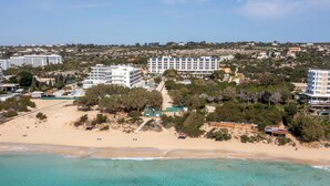 Eine Luftaufnahme einer Küstenregion mit Strand, mehreren Gebäuden und einem klaren, blauen Meer.