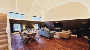 A spacious living room with a wooden floor, a dining area with a table and chairs, a sofa set, a TV mounted on the wall, and a staircase on the left. - Unique town centre apartment with vaulted ceiling - Pass the Keys (Shrewsbury)