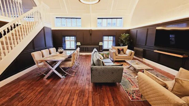 A spacious living area with a wooden floor, a staircase, a sofa set, a coffee table, and a television. - Unique town centre apartment with vaulted ceiling - Pass the Keys (Shrewsbury)