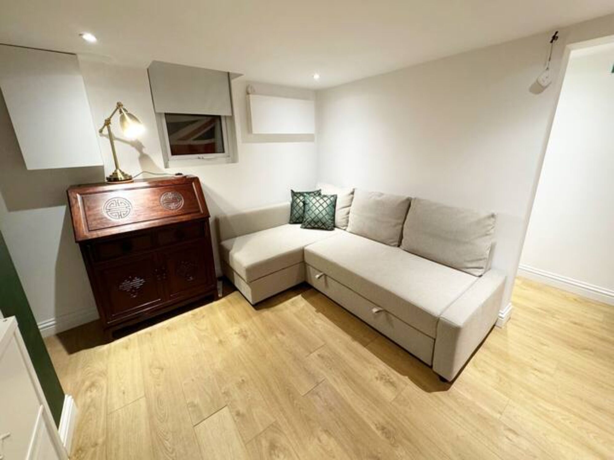 A corner room with a wooden dresser, a beige sofa, and a small window.
