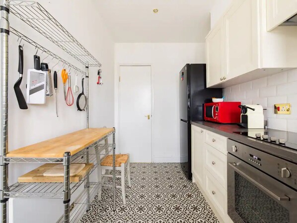 A compact kitchen with a wooden countertop, a red microwave, a black refrigerator, and a patterned floor.