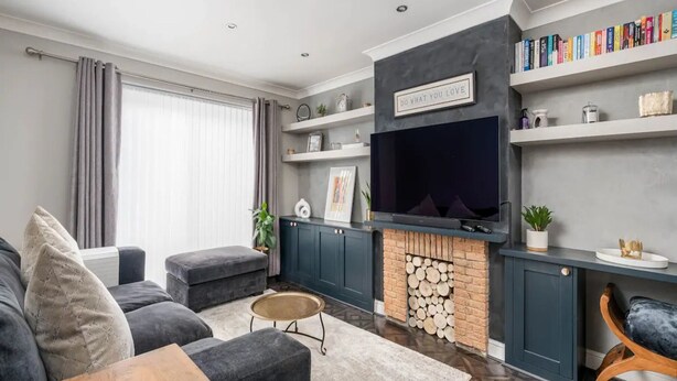 A modern living room with a fireplace, grey sofas, a TV, and bookshelves.