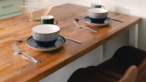 A dining table with two bowls and two cups, each with a matching saucer, and two forks.