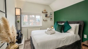 A neatly arranged bedroom with a large bed, a bedside table, a lamp, and a window with a view of buildings outside.
