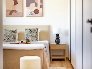 A neatly arranged hotel room with a bed, two patterned pillows, a bedside table with a lamp, and artwork on the wall. - Sanders Florida - Exquisite 1-bdr Apt w Sea View (Ayia Napa)