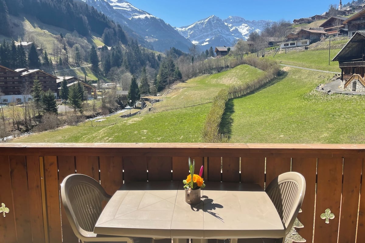 A balcony with a table and chairs overlooking a mountainous landscape with houses and a church.