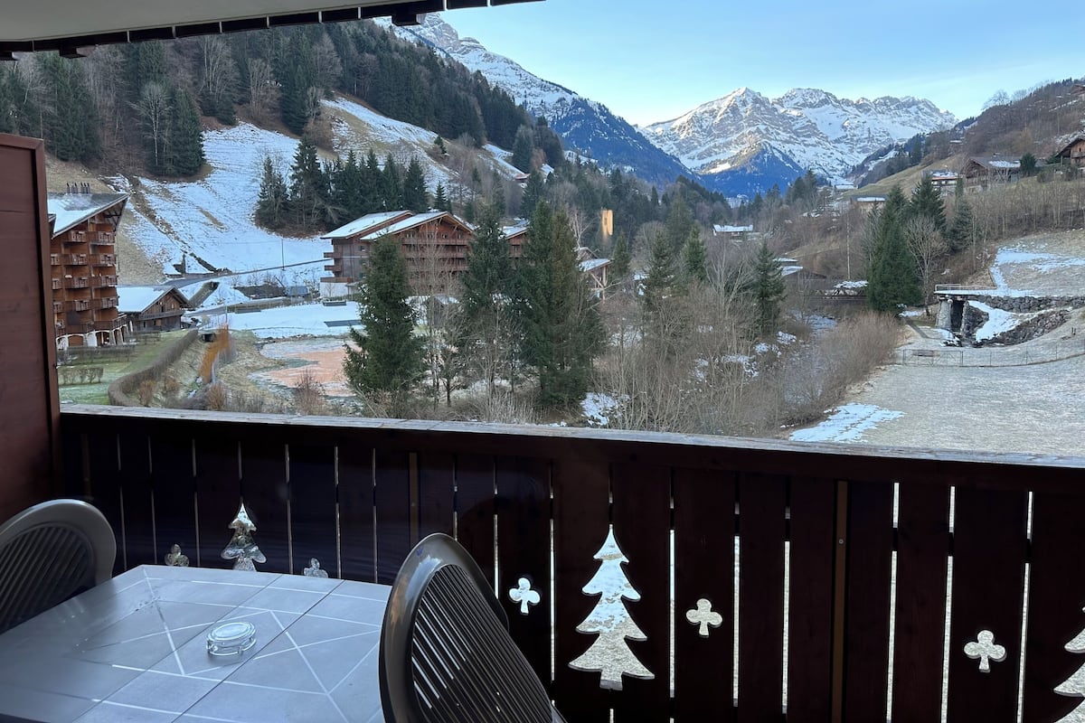 A room with a view of snow-covered mountains, a wooden table, and a chair.