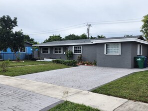 A single-story house with a grey exterior, a paved driveway, and a small front yard with a tree and shrubs. - The Perfect Vacation Getaway ! (Miami)