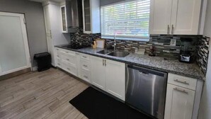 A modern kitchen with white cabinets, a stainless steel dishwasher, and a granite countertop. - The Perfect Vacation Getaway ! (Miami)
