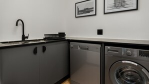 A compact kitchen with a sink, dishwasher, and a washing machine. There are two framed pictures on the wall. - Comfort and Style With Stunning Table Mountain View (Cape Town)