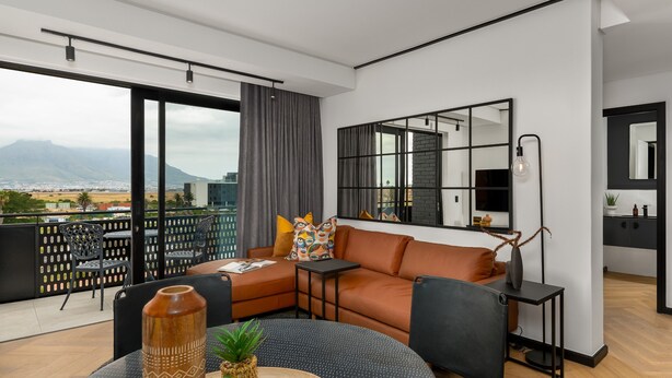 A modern living room with a large window, a sofa, a coffee table, and a dining area. - Comfort and Style With Stunning Table Mountain View (Cape Town)