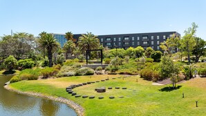 A landscaped garden with a pond, a circular seating area, and a modern building in the background. - Comfort and Style With Stunning Table Mountain View (Cape Town)