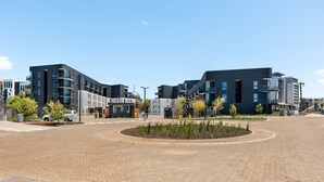 Una plaza urbana moderna con edificios contemporáneos, superficie pavimentada y escasa vegetación.