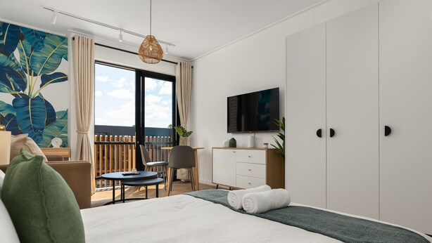 Una habitación de hotel moderna con una cama grande, un escritorio, una silla, un televisor y un balcón con vistas.