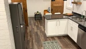 Een moderne keuken met houten vloer, witte kastjes, een zwart aanrecht en een klein bijzettafeltje.