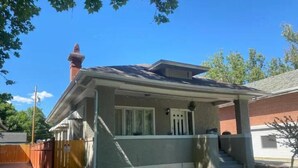 Een gelijkvloers huis met een veranda, schoorsteen en een kleine voortuin.