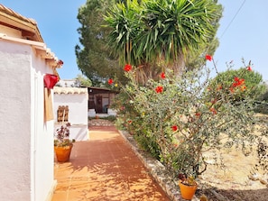 Un chemin mène à un bâtiment blanc, orné d’un pot de fleurs rouge et doté d’une porte en bois.