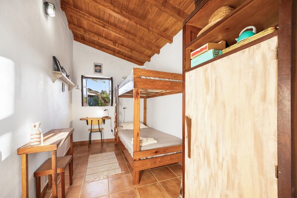 Una habitación con literas, un escritorio, una silla, una mesita y una ventana con vistas a la vegetación.
