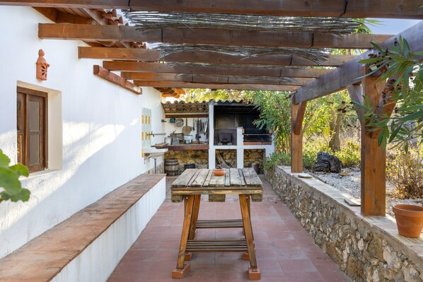 A rustic outdoor patio with a wooden table, a stone wall, and a pergola structure.