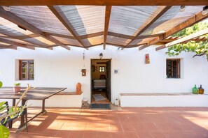 A covered patio area with a table and chairs, a small potted plant, and a door leading to an interior space. - Rural Retreat Near Lagos – Private Garden – Family Friendly – Pet Friendly (Bensafrim)