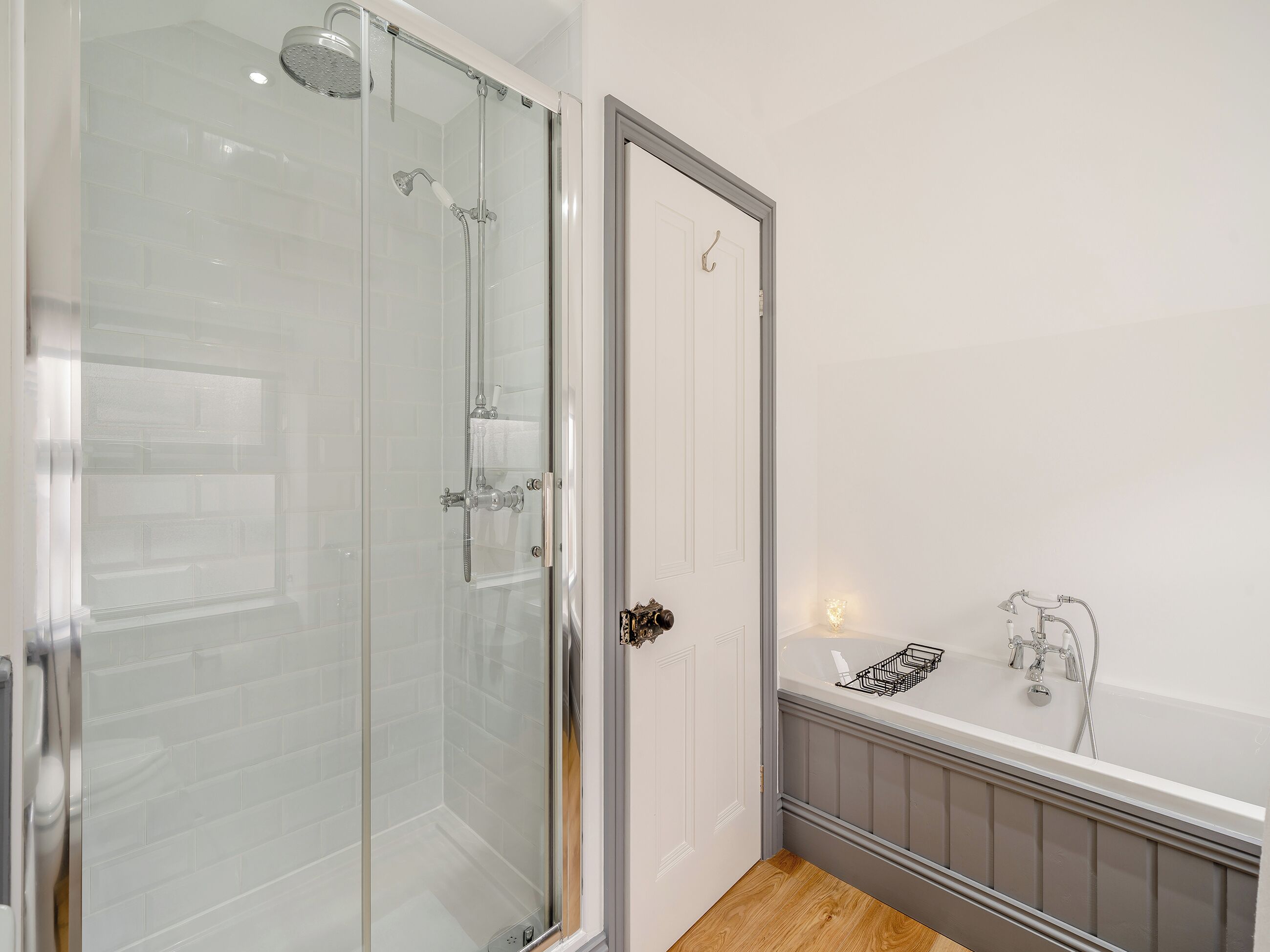 A modern bathroom with a glass-enclosed shower, a white door, and a bathtub with a small shelf.