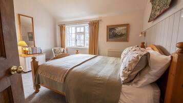 A bedroom with a bed, a nightstand, a lamp, a window with curtains, a painting on the wall, and a door.