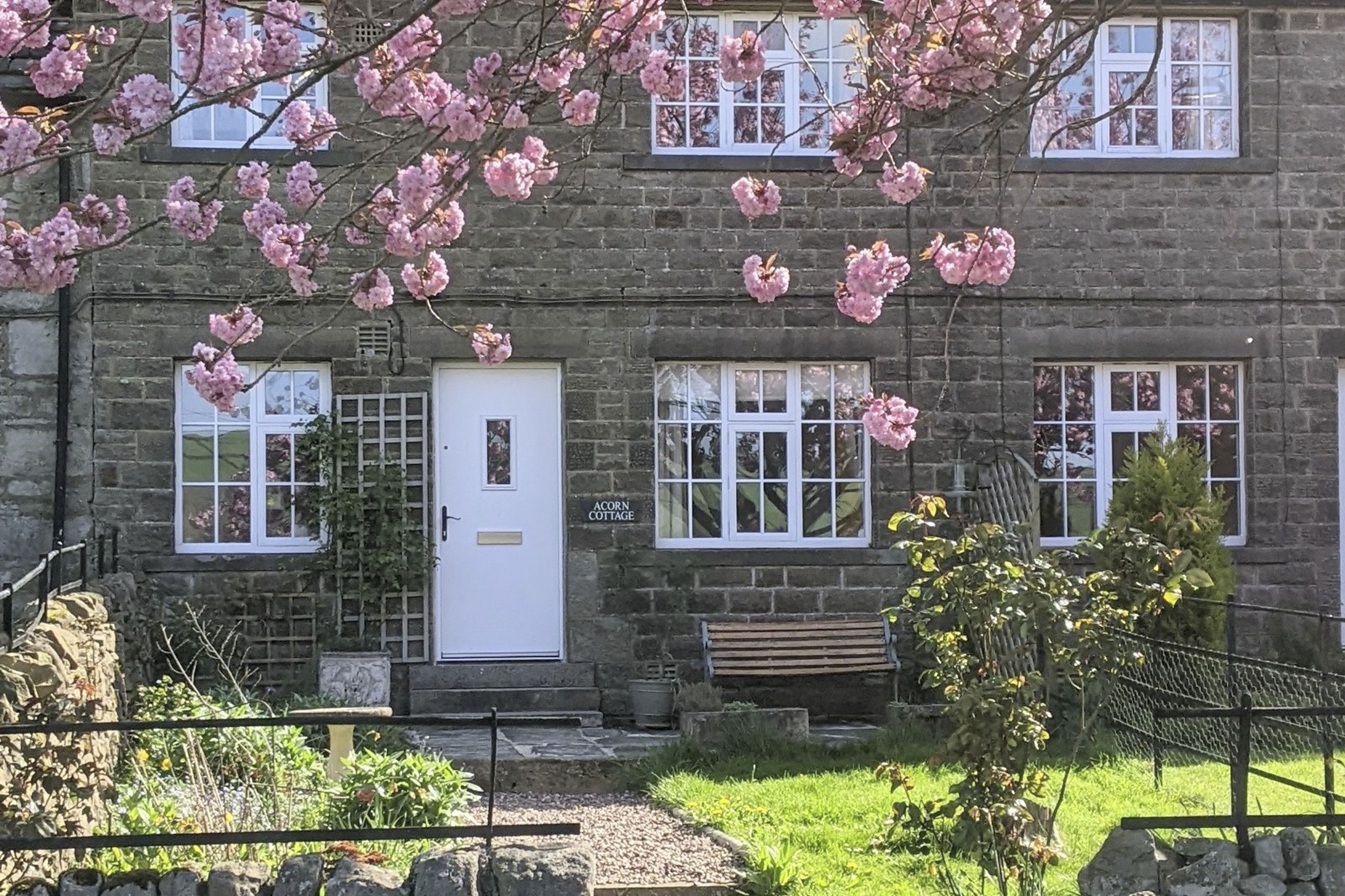 Une petite maison en pierre avec une porte blanche, de nombreuses fenêtres et un petit porche à l’avant.