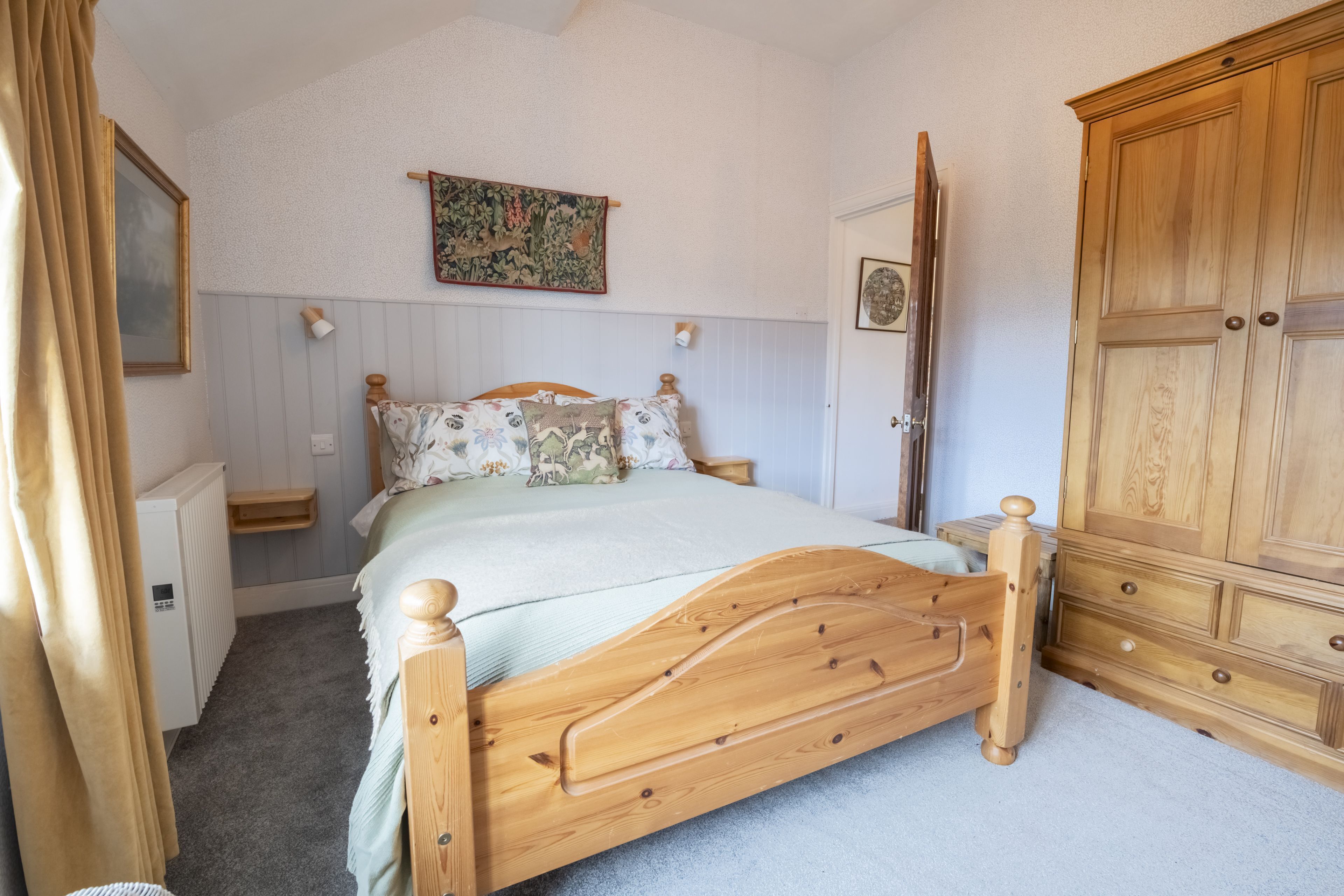 A bedroom with a wooden bed, a wardrobe, a radiator, and a wall-mounted tapestry.