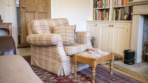 A living room with a plaid armchair, a wooden coffee table, a patterned rug, a bookshelf with books, and a fireplace. - Acorn Cottage, Bolton Abbey, Yorkshire Dales (Beamsley, Skipton)