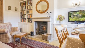A cozy living room with a fireplace, bookshelves, a television, and a dining area. - Acorn Cottage, Bolton Abbey, Yorkshire Dales (Beamsley, Skipton)