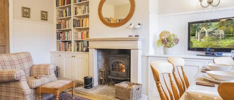 A cozy living room with a fireplace, bookshelves, a television, and a dining area.